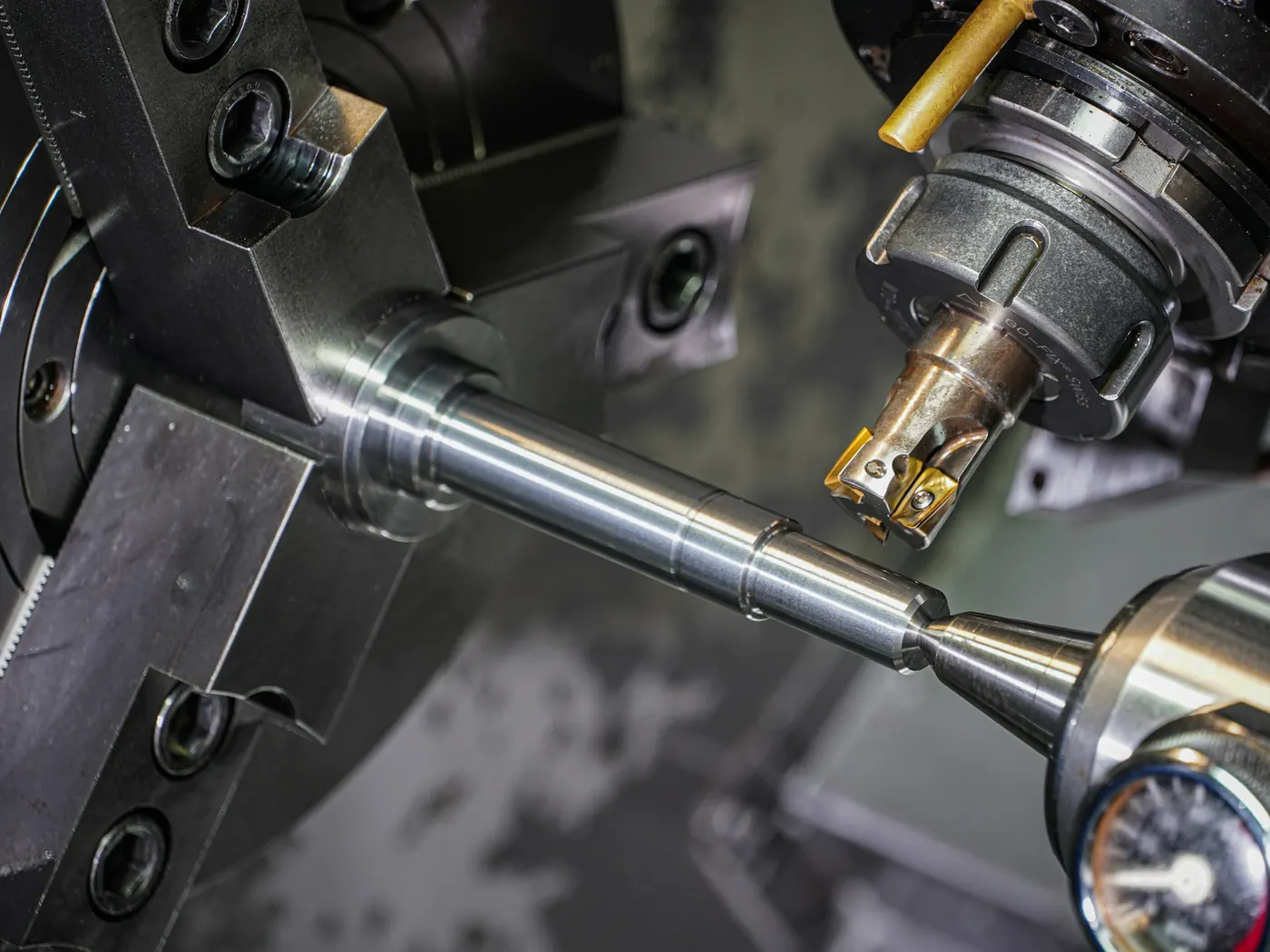 Steel shaft held in a lathe chuck and supported by a tailstock centre, with an indexable milling cutter positioned beside it
