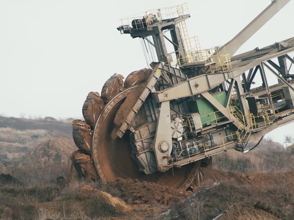 Bucket wheel of a bucket-wheel excavator cutting into brown overburden, with the boom structure and access walkways behind