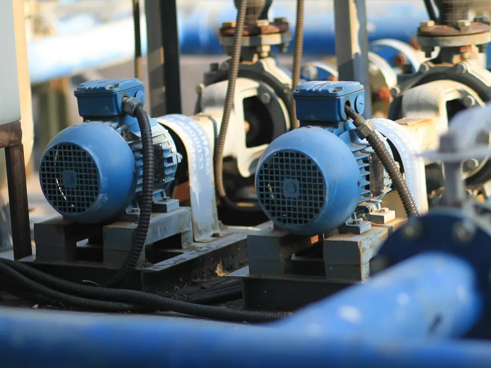 Two blue electric motors on steel base frames driving pumps, with armoured cables and blue flanged pipework around them