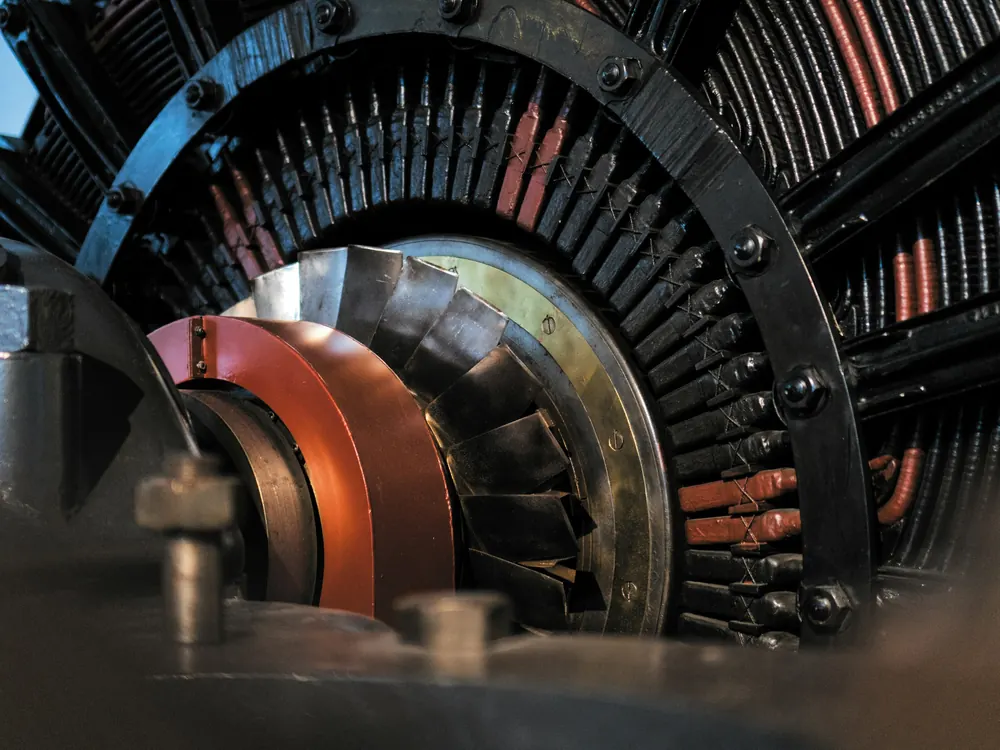 Close-up of the rotor end of a large electrical machine showing a copper slip ring, fan blades and bolted winding supports